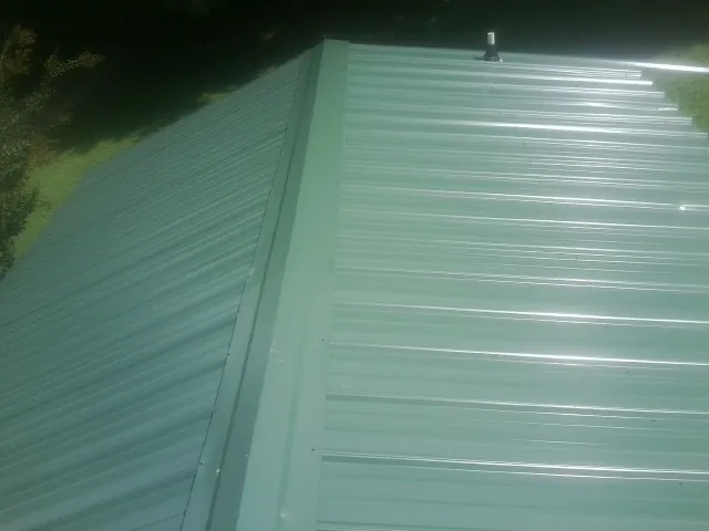 New green metal panels meeting at the ridge of a roof — Flat Roof Repair work by our crew in Havana