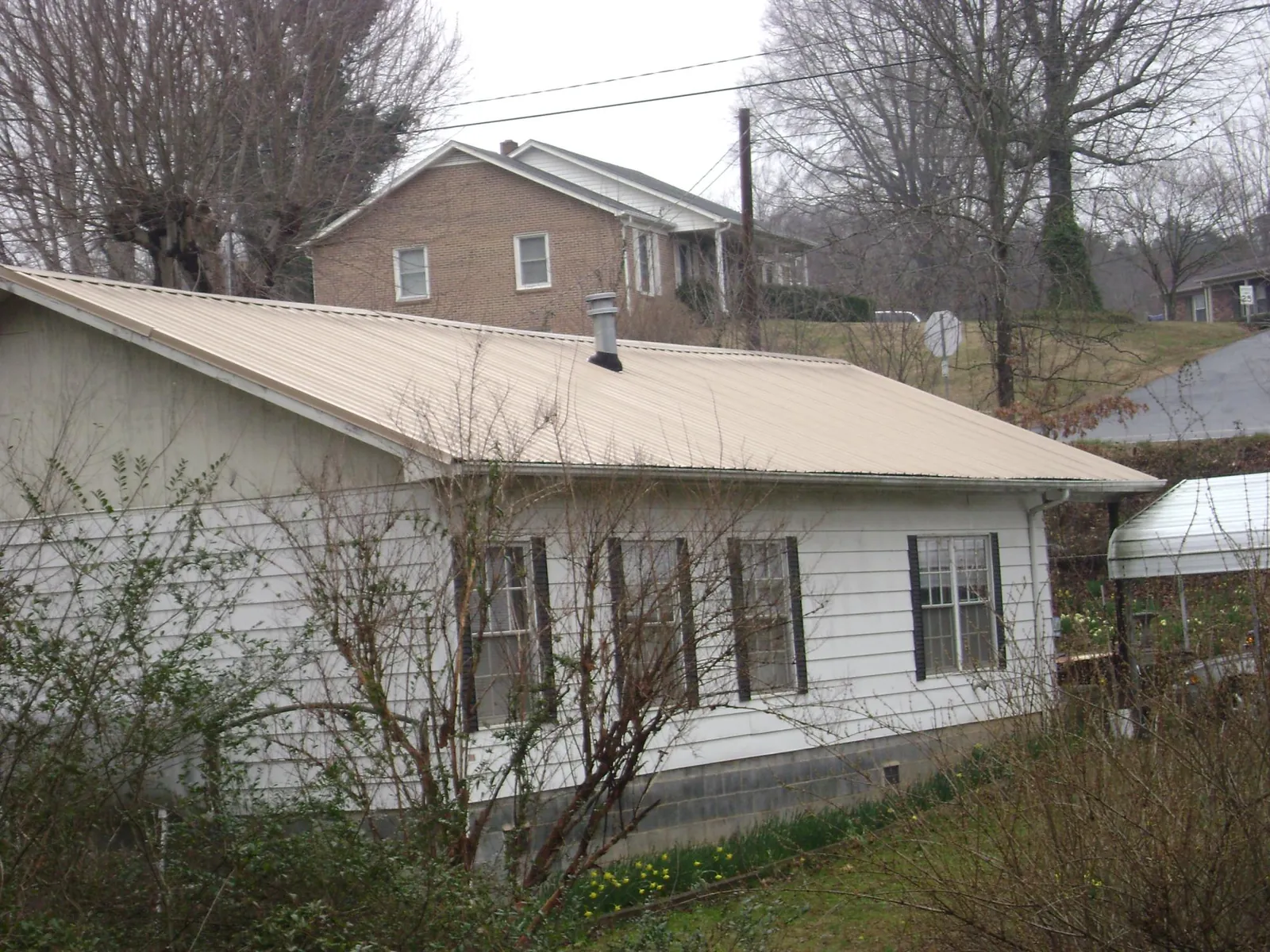 Tan metal roof on a white sided house set into a hillside — Commercial Roofing by Roofing Brothers in Havana